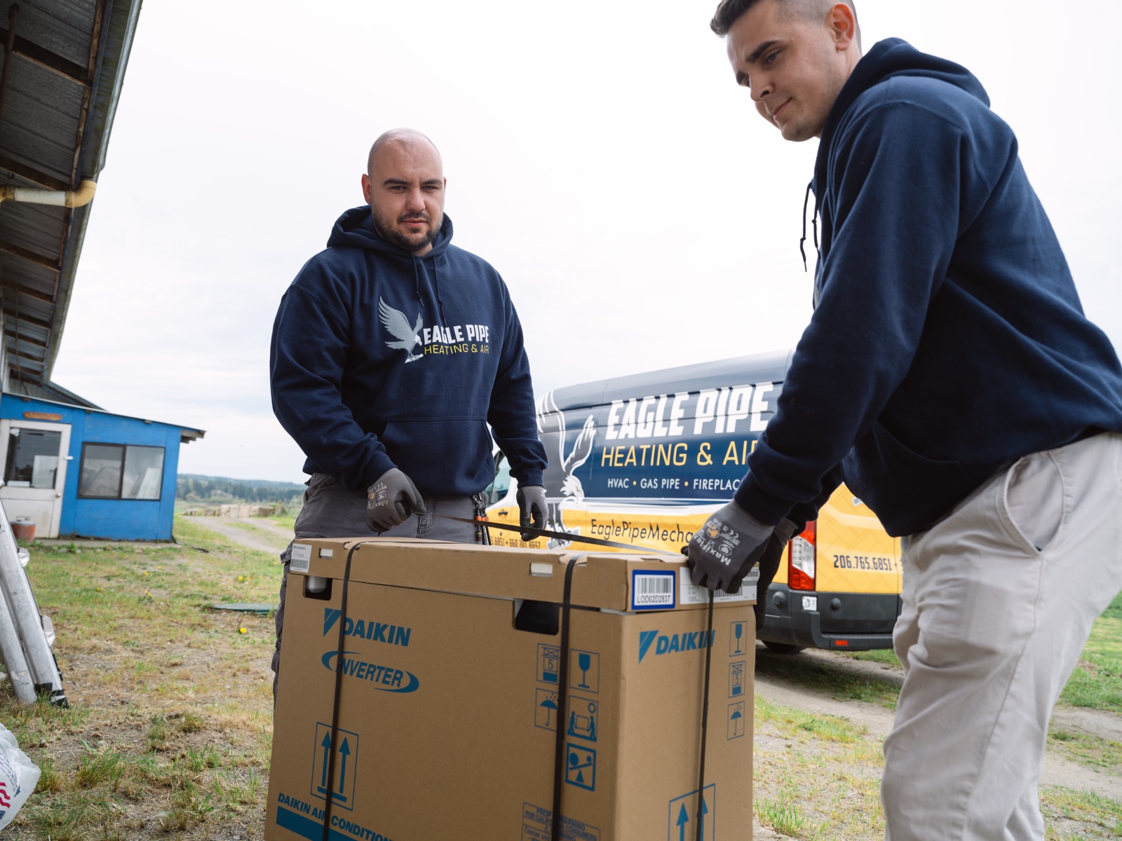 Two Eagle Pipe technicians lifting a new Daikin unit out of the service van at a donation install
