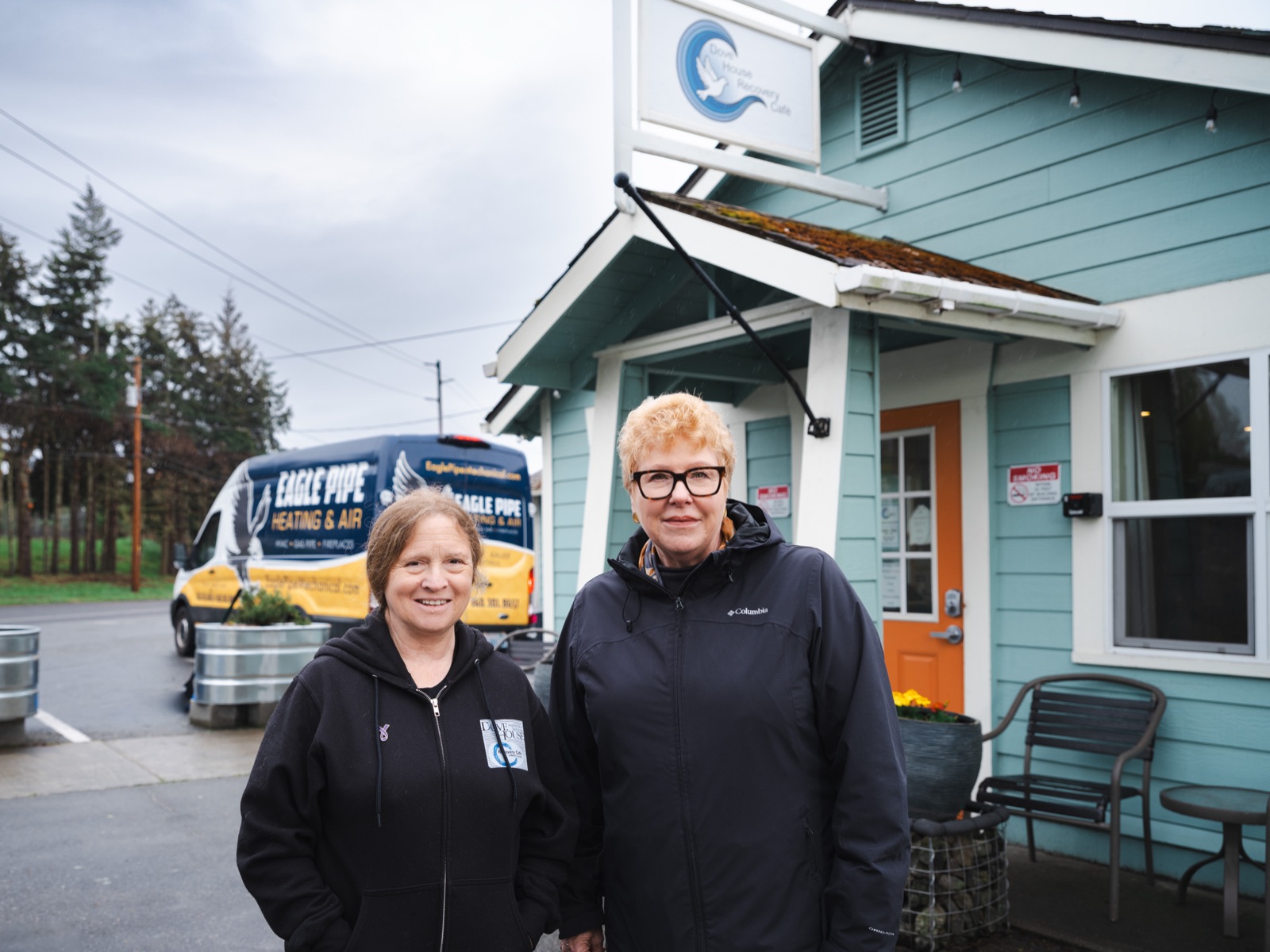 Lori Tschohl with a Dove House Recovery Cafe staff member outside the cafe, an Eagle Pipe service van parked behind them