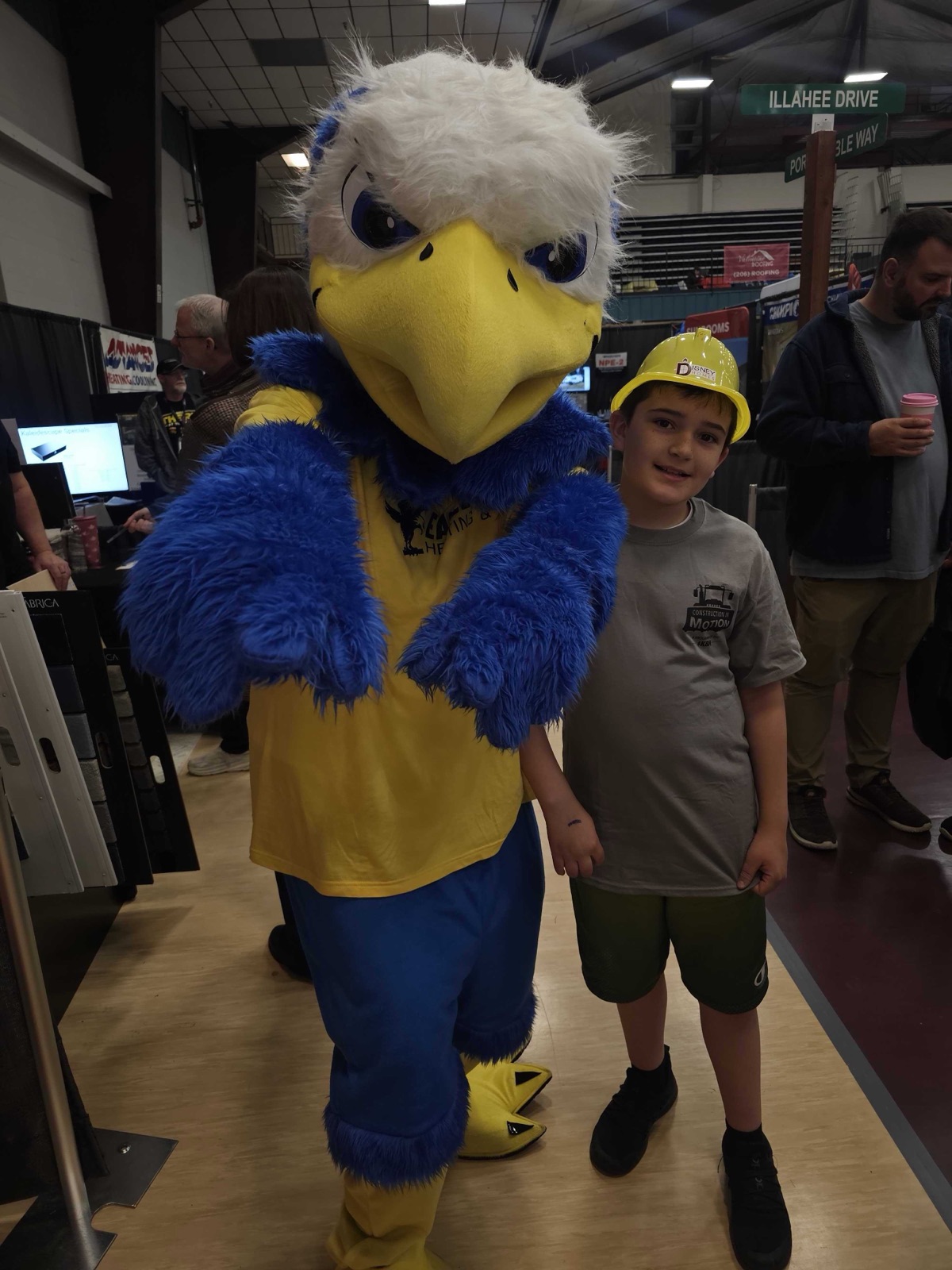 The Eagle Pipe mascot posing with a young visitor in a hard hat at the home show