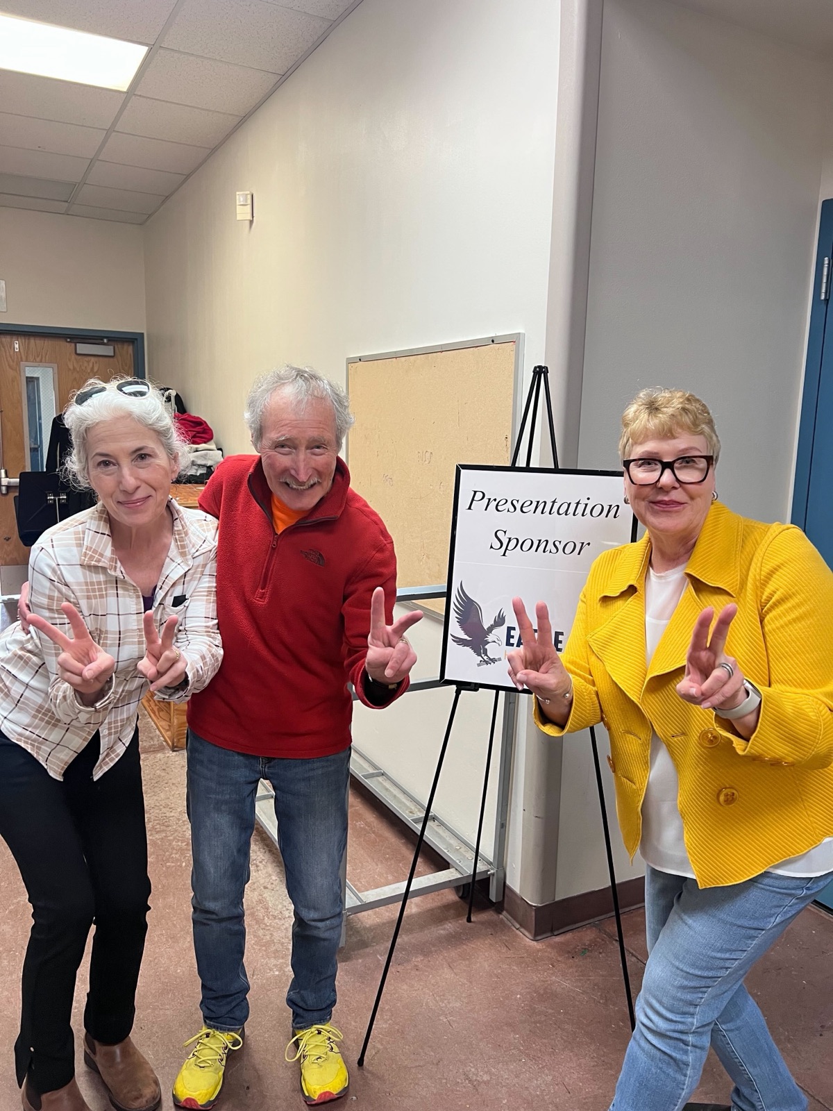 Three event organizers throwing peace signs beside a Presentation Sponsor sign carrying the Eagle Pipe logo