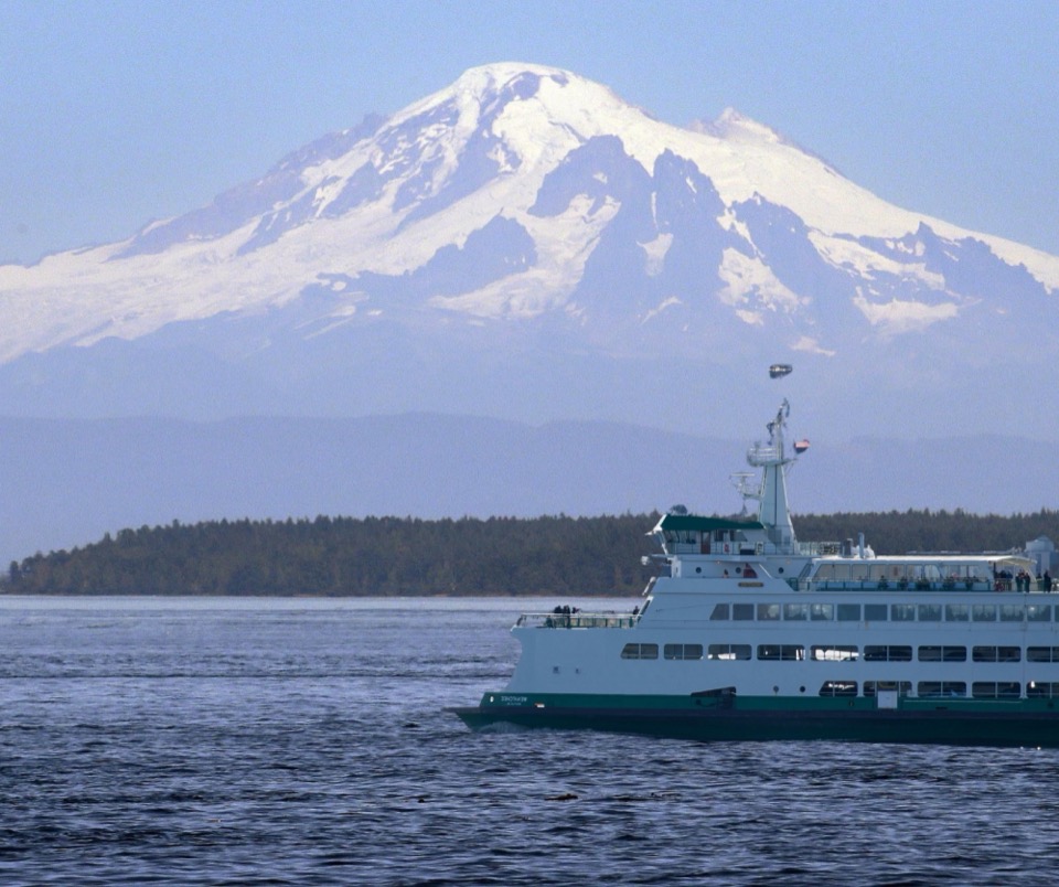 A Washington State ferry crossing Puget Sound toward Bainbridge Island, with a snow-capped volcano rising behind it