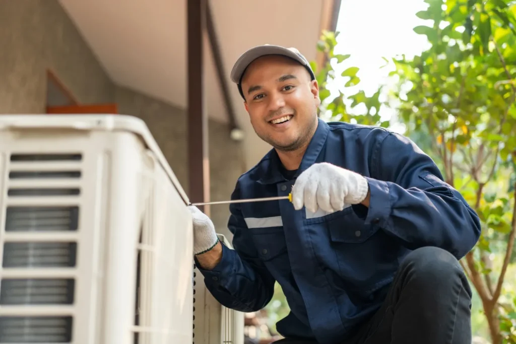 AC Replacement In Silverdale, WA 1 HVAC Technician wearing proper blue clothing with gloves and cap who is trying to replace an outdoor AC with a tool